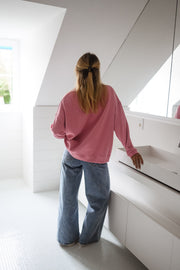 Pull loose à col rond porté par une femme, vue de dos, escalier blanc, jean large
