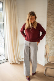 Pull doux légèrement court bordeaux porté par une femme, vue de face, pantalon gris, rideaux
