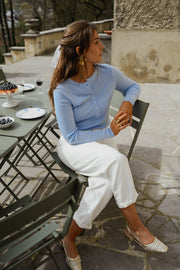 Pull boutonné à manches longues porté par une femme, assise, sur une chaise de jardin, jambes croisées