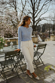 Pull boutonné à manches longues porté par une femme, silhouette entière, pantalon blanc, terrasse