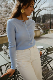 Pull boutonné à manches longues porté par une femme, vue de trois-quarts, pantalon blanc, boucles d'oreilles