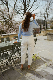 Pull boutonné à manches longues porté par une femme, vue de dos, pantalon blanc, terrasse