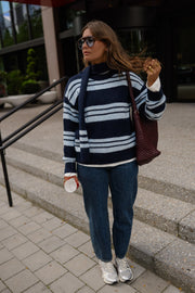 Pull doux avec écharpe porté par une femme, vue de trois-quarts, sac sur l'épaule, sur des marches