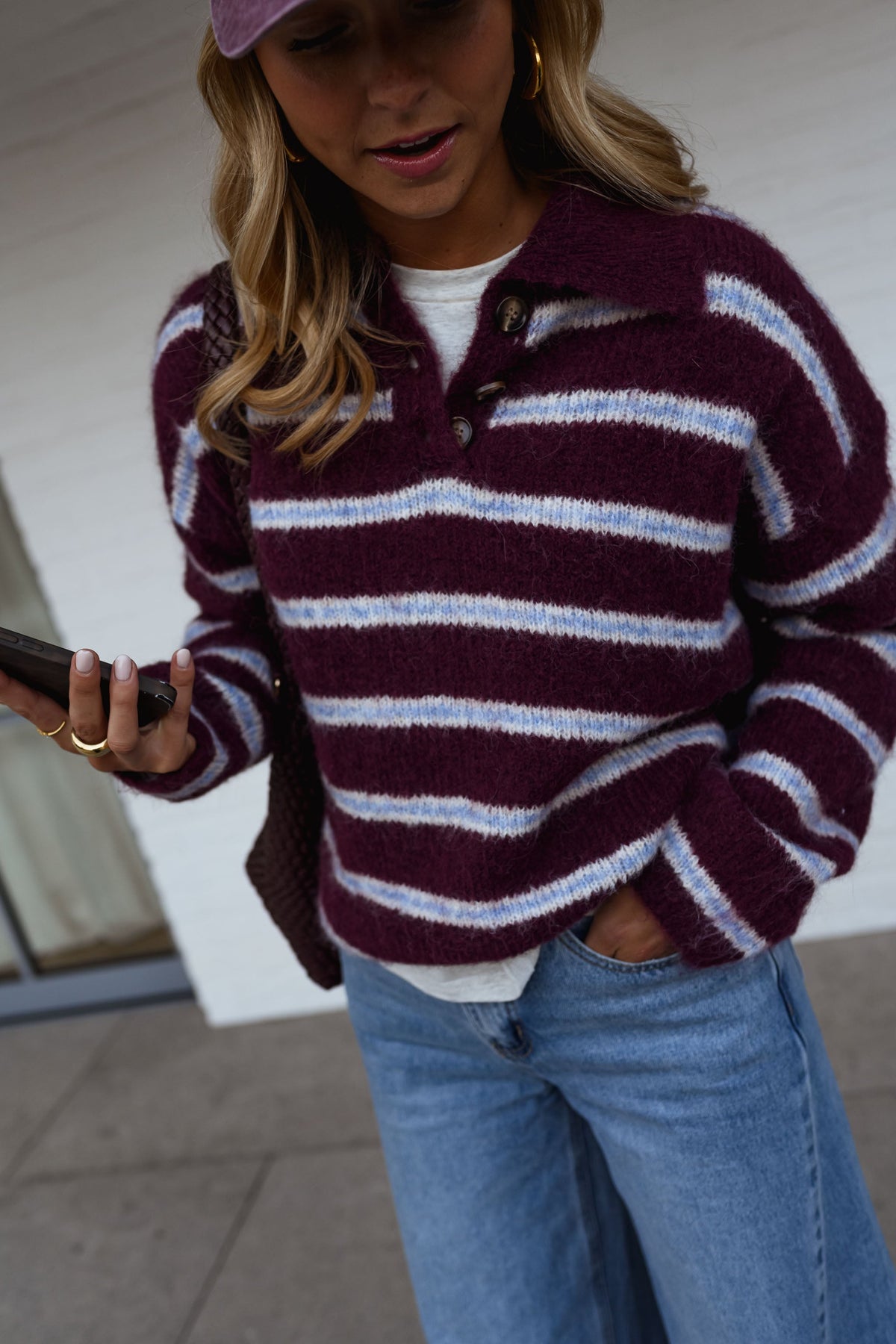 Pull doux à col revers porté par une femme, vue rapprochée, rayures bordeaux, téléphone