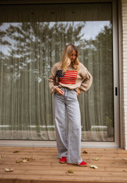 Pull à drapeau col rond camel porté par une femme, silhouette entière, baie vitrée, baskets rouges