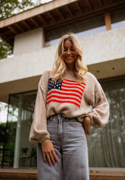 Pull à drapeau col rond camel porté par une femme, vue de face, drapeau, terrasse
