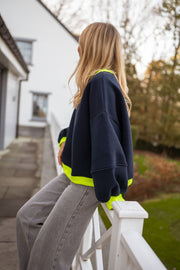 Pull ample à finitions contrastées bleu porté par une femme, vue de profil, escalier de la terrasse, cheveux longs