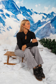 Pull moulant à col revers noir porté par une femme, assise, traîneau, bottines