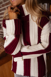 Pull rayé à col roulé porté par une femme, silhouette entière, bottes, canapé