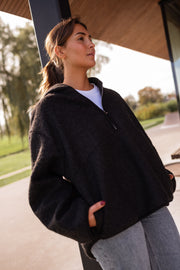Pull ample zippé à capuche noir porté par une femme, vue de profil, capuche, terrasse