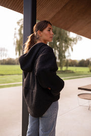Pull ample zippé à capuche noir porté par une femme, vue rapprochée, col zippé, détail