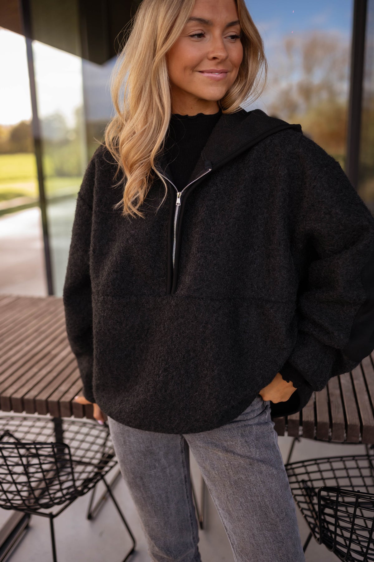 Pull ample zippé à capuche noir porté par une femme, vue rapprochée, zip, jean gris