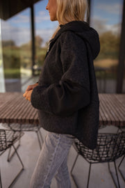 Pull ample zippé à capuche noir porté par une femme, vue de dos, cheveux blonds, extérieur