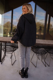 Pull ample zippé à capuche noir porté par une femme, vue de dos, capuche, table