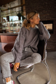 Pull doux et ample gris porté par une femme, assise, chaise, jean gris