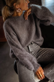 Pull doux et ample gris porté par une femme, vue rapprochée, main sur le menton, queue de cheval