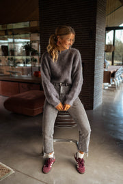 Pull doux et ample gris porté par une femme, vue de face, chaussures bordeaux, bibliothèque