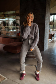 Pull doux et ample gris porté par une femme, vue de face, chaussures bordeaux, jean