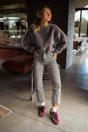 Pull doux et ample gris porté par une femme, vue de face, jean gris, mains dans les poches