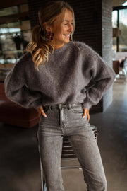 Pull doux et ample gris porté par une femme, vue de trois-quarts, main dans la poche, jean