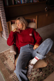Pull doux légèrement ample bordeaux porté par une femme, assise, fauteuil, jean, chaussettes à rayures