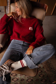 Pull doux légèrement ample bordeaux porté par une femme, assise, fauteuil, jambes croisées, chaussettes