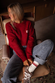 Pull doux légèrement ample bordeaux porté par une femme, assise, fauteuil, lacets, chaussettes