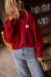Pull doux légèrement ample bordeaux porté par une femme, vue rapprochée, étiquette brodée, sourire