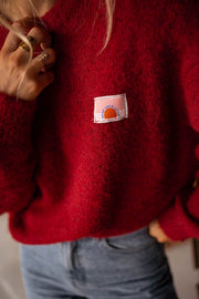 Pull doux légèrement ample bordeaux porté par une femme, vue rapprochée, étiquette brodée, détail