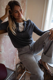 Pull à col revers boutonné gris porté par une femme, assise, tabouret, jean gris