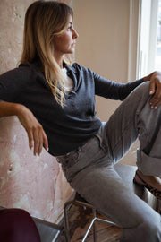 Pull à col revers boutonné gris porté par une femme, assise, tabouret, mur patiné