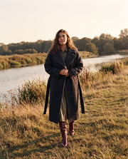 Manteau oversize en laine porté par une femme, silhouette entière, bottes bordeaux, rivière