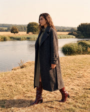 Manteau oversize en laine porté par une femme, en marchant, bottes bordeaux, rive