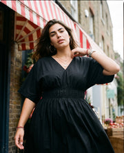 Robe midi évasée en popeline portée par une femme, vue de trois-quarts, store rouge, rue