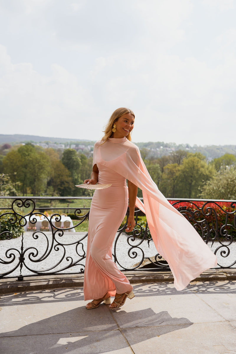 Robe longue moulante drapée portée par une femme, silhouette entière, balcon fer forgé, cape