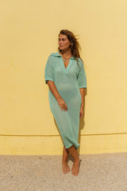 Robe en maille ajourée portée par une femme, vue de face, mur jaune, mains jointes
