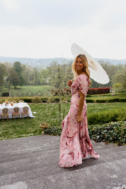 Robe longue col bardot portée par une femme, silhouette entière, parasol blanc, jardin