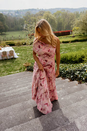 Robe longue col bardot portée par une femme, vue de trois-quarts, cheveux au vent, jardin