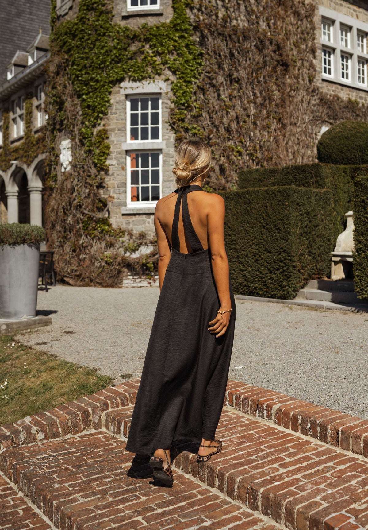 Robe fluide à dos ouvert portée par une femme, vue de dos, allée en brique, jardin