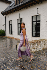 Robe asymétrique en soie fendue portée par une femme, silhouette entière, façade blanche, sac