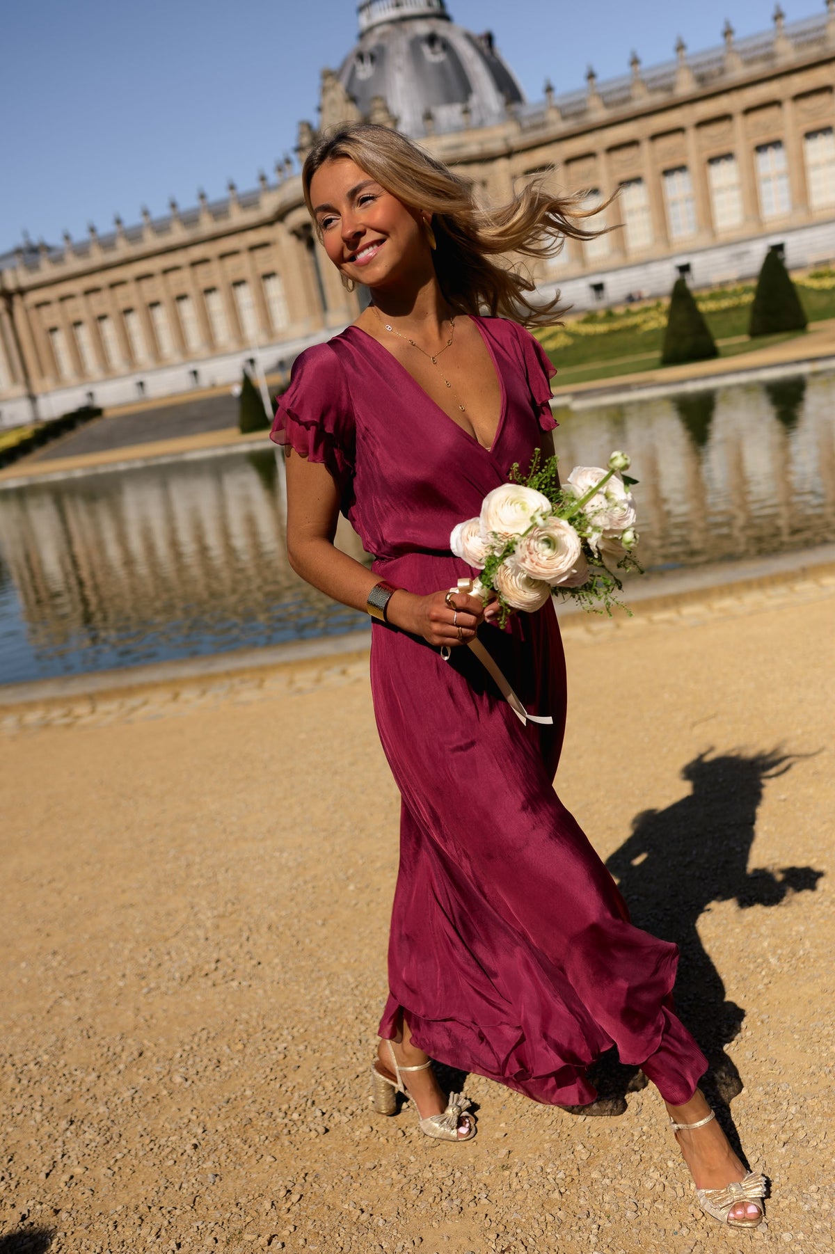Robe longue en soie cache-cœur portée par une femme, vue de trois-quarts, bouquet blanc, château