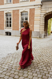 Robe longue en soie asymétrique portée par une femme, en marchant, façade en brique, gravier