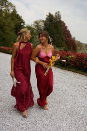 Robe longue en soie asymétrique portée par une femme, Deux femmes en robe longue framboise sur une allée de gravier, bouquet de fleurs jaunes