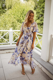 Robe portefeuille fleurie longue portée par une femme, vue de face, balustrade, sourire