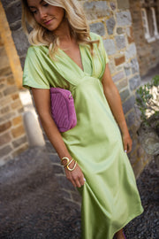 Robe satinée à col plissé portée par une femme, vue de trois-quarts, pochette violette, mur en pierre