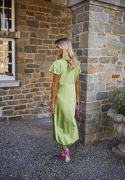 Robe satinée à col plissé portée par une femme, vue de dos, mur, cheveux blonds