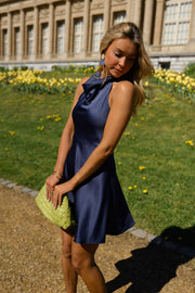 Robe fluide courte dos nu portée par une femme, silhouette entière, pelouse, pochette verte