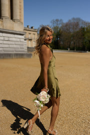 Robe courte satinée drapée portée par une femme, en marchant, sable, bouquet blanc