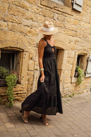Robe longue effet lin portée par une femme, vue de face, chapeau de paille, mur en pierre