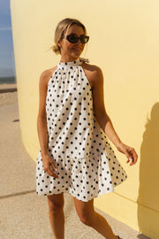 Robe à pois col montant portée par une femme, silhouette entière, mur jaune, plage